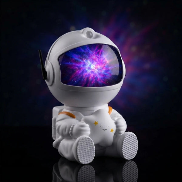A white astronaut-shaped night light or toy with a colorful purple and blue galaxy print on the visor, sitting on a reflective black surface against a dark space background.